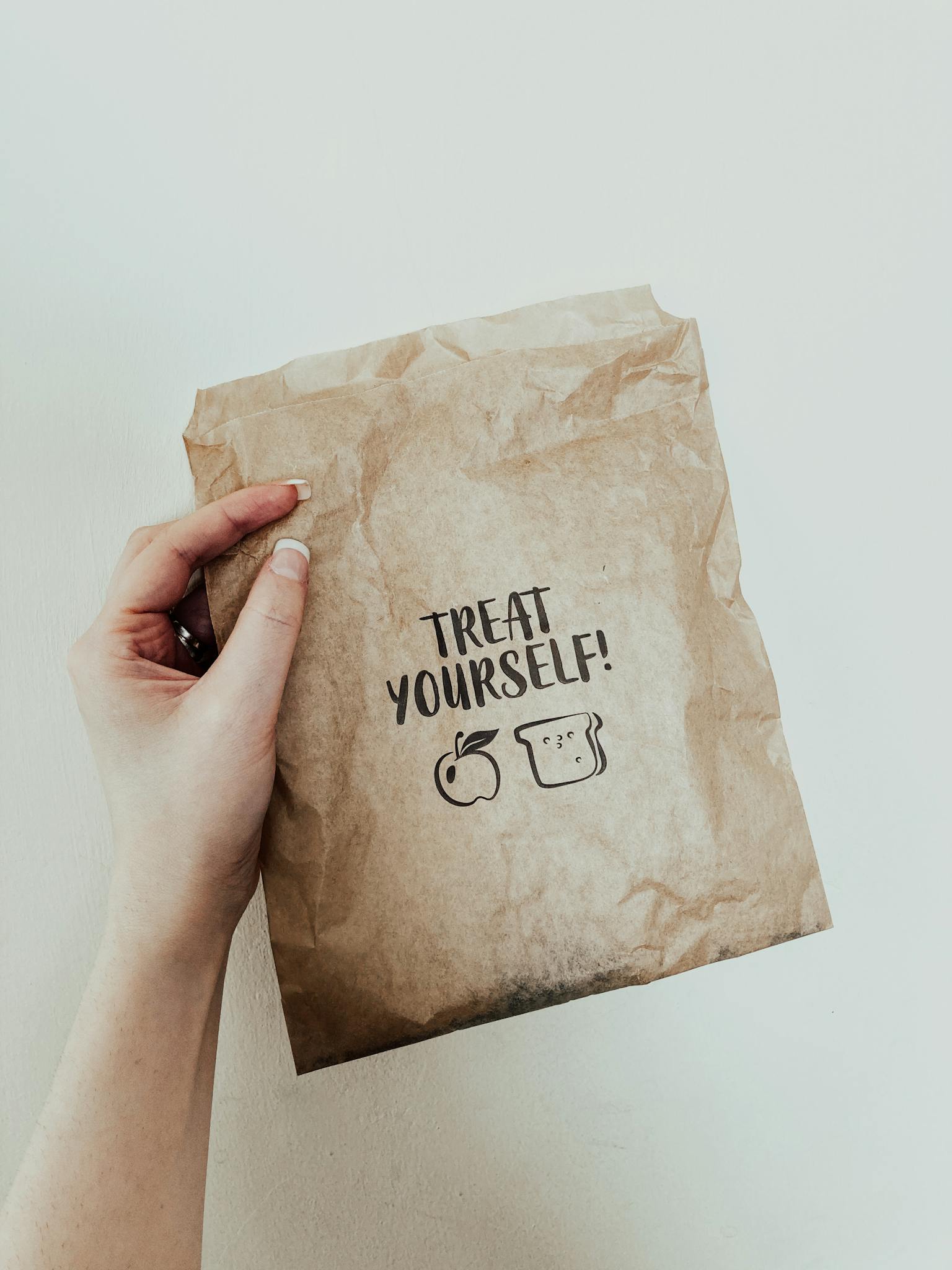 Hand holding a kraft paper grocery bag with 'Treat Yourself' and food icons for eco-friendly message.